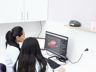 Two female dentists in a clinic reviewing 3D dental images on a computer for precise diagnostic evaluations.